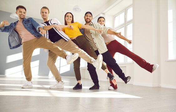 Happy dancers posing for a photo standing in a row on one leg. Cheerful friends having fun together during a dancing class. Low angle group shot of smiling young people walking in line in single file