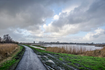 Fototapeta na wymiar Narrow asphalt bicycle road under a dramatic sky in Krimpenerwaard polder in the Netherlands