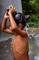 Fototapeta premium Closeup of a child taking bath with a mug. A kid pouring water with a jug and splashing water over head.
