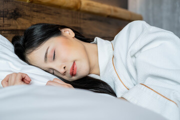 Young Asian woman with lying in bed under white cover in the morning. Young pretty lady sleeping in bed. Young woman on bed in modern apartment. Woman stretching in bed after wake up.