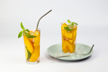 Refreshing summer drink. Peach juice or tea with peach slice, ice cube, straws and mint on white background.