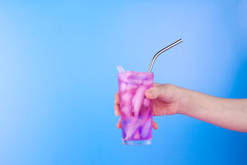 Female hand with pink cold refreshing cocktail in glass on blue background. Summer drink background with copy space.