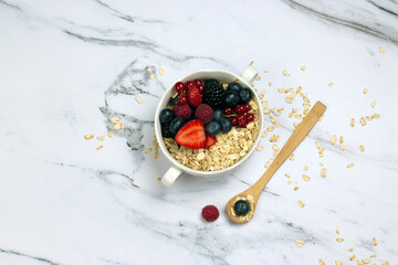 Healthy breakfast, oat with berry and wooden spoon on white marble table. top wave, flat lay.