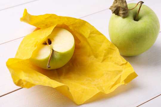 Half of apple in yellow beeswax food wrap on white wooden table