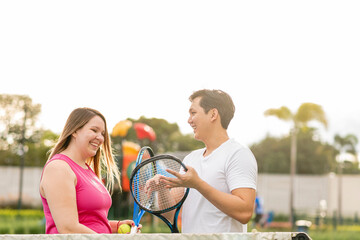 Hombre asiático explicando a una mujer caucásica, cómo utilizar las raquetas para jugar tenis	
