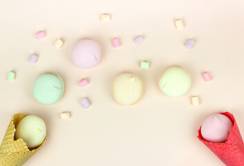 Red and yellow waffle cone with green, pink and yellow marshmallows looks like macaroons on pastel background. Top view, sweets and festive candy concept.
