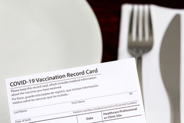 Covid-19 vaccination card and restaurant table. Indoor vaccine mandate, entertainment restrictions and vaccination requirement concept.