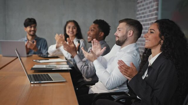 Satisfied diverse employees sitting in conference room listen colleague presentation clap hands in meeting happy audience applauding after training workshop business people rejoice corporate success