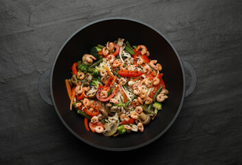Stir fried noodles with mushrooms, shrimps and vegetables in wok on black table, top view