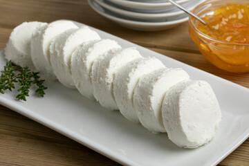 Row of white soft small goat cheese on a plate for a snack with sweet marmelade for topping in the background 