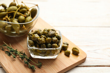 Tasty capers and thyme on white wooden table, space for text