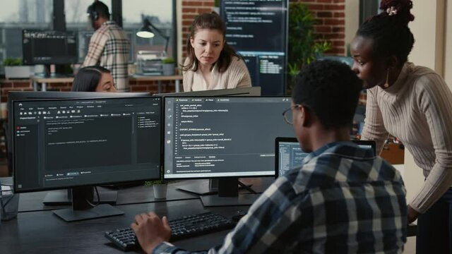 Mixed team of artificial intelligence cloud programers talking about programming in front of multiple screens compiling code. Programmers doing teamwork looking at machine learning algorithms.