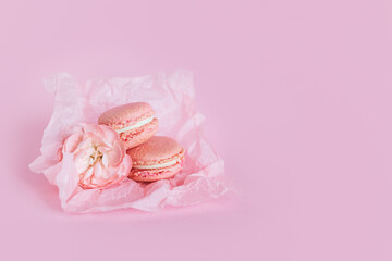 Tasty french macaroons with flowers on a pink pastel background.