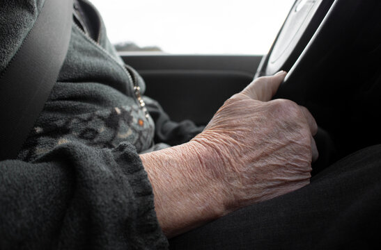 Old Man Hand With Wrinkles Is Holding The Steering Wheel While Driving. Close Up.