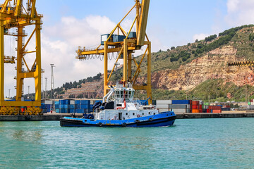 Fototapeta premium Tugboat in the port of Barcelona with large container unloading cranes.