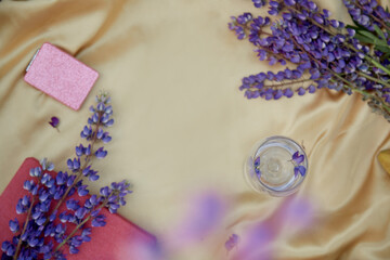 Lupins purple flowers and wine glass decorations on golden background. Summer invitation, birthday card, Mother's day concept. Place for text. Wellness closeness to nature concept