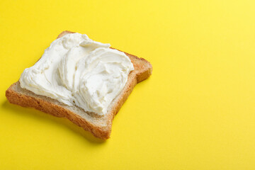 Slice of bread with tasty cream cheese on yellow background, space for text