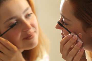 Woman painting eyelashes looking in mirror