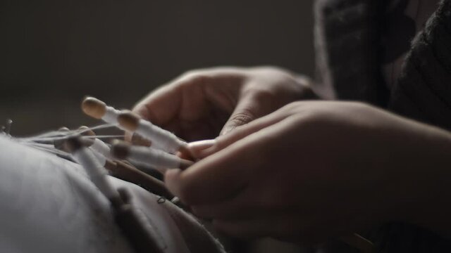 Female hands weaving and tightening lace threads with bobbins in a backlight