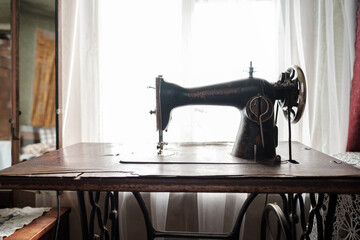 Vintage mechanical sewing machine with a table stands by a window in a rustic house.