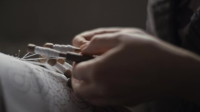 Detail close-up of female hands weaving and tightening lace threads with bobbins