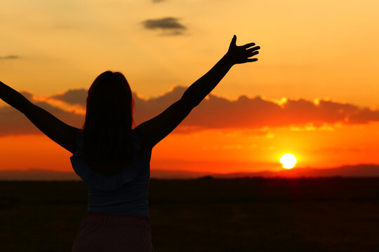 Silhouette of a woman outstretching arms at sunset