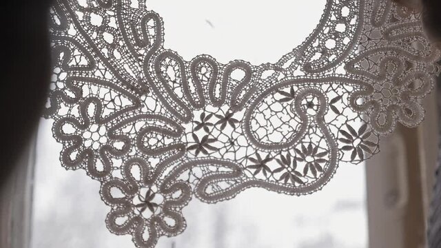 close-up of woman's hands raising embroidered lace in front of the window