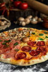 Italian Pizza Four Seasons (Pizza Quattro Stagioni) with different ingredients on the wooden table in the kitchen