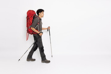 Full length portrait of Asian man with a backpack and hiking poles walking isolated on white...