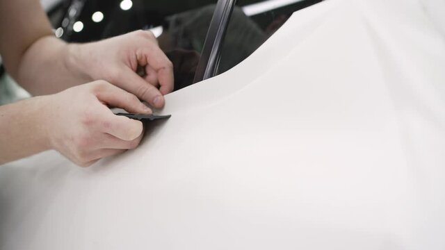 Detailing the car. The master sticks a white protective film on the car body. Applying a white protective film to the car. Close-up of installation of a protective film of a modern luxury car.