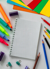 Open notebook and school supplies on a white background. Notebook, colored paper, pencils, markers and paper clips, Copy space.