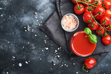 Glass of fresh tomato juice, salt, basil and tomatoes on black plate on old black background. Top view with copy space.