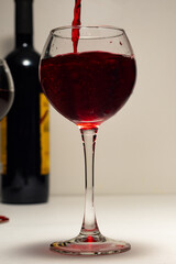 The glass, close-up, is filled with red wine. A glass of red wine, a bottle, a light background and a bokeh of lights. A postcard for holidays and dinners.
