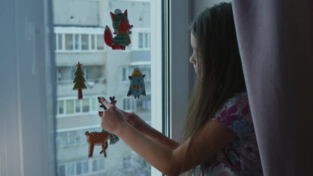 Smiling little girl spraying synthetic artificial snow on the window to decorate for the holiday.