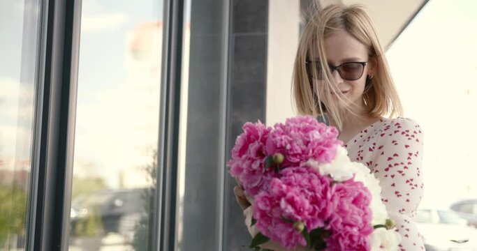 Pretty blonde woman holding a bunch of peonies