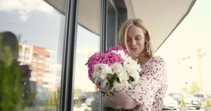 Pretty blonde woman holding a bunch of peonies