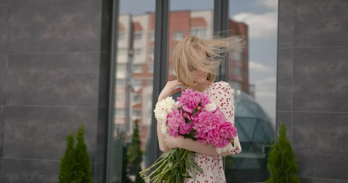 Pretty blonde woman holding a bunch of peonies