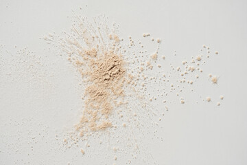 Beauty, skincare product setting. Neutral beige cosmetic powder sprinkled on white background