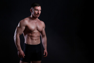 Fototapeta na wymiar Professional bodybuilder posing over isolated black background. Studio shot of a fitness trainer flexing the muscles. Close up, copy space.