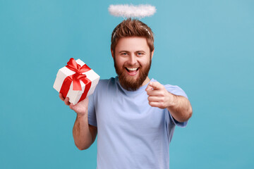 Portrait of bearded angelic man with holy nimbus with kind smile holding gift box, charity...