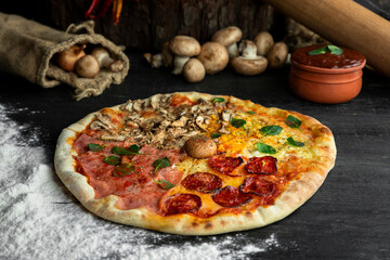 Italian Pizza Four Seasons (Pizza Quattro Stagioni) with different ingredients on the wooden table in the kitchen