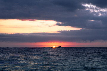 Fototapeta na wymiar Pescador en su barco al amanecer en el mar