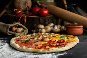 Italian Pizza Four Seasons (Pizza Quattro Stagioni) with different ingredients on the wooden table in the kitchen
