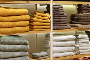 Neatly folded towels by color on wooden shelves, sale of towels in soft colors