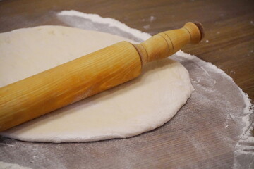 A wooden rolling pin lies on a rolled yeast dough on a wooden table in flour.
