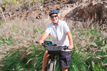 Happy senior man riding in a country road with his bike, cyclist wearing sport helmet and sunglasses