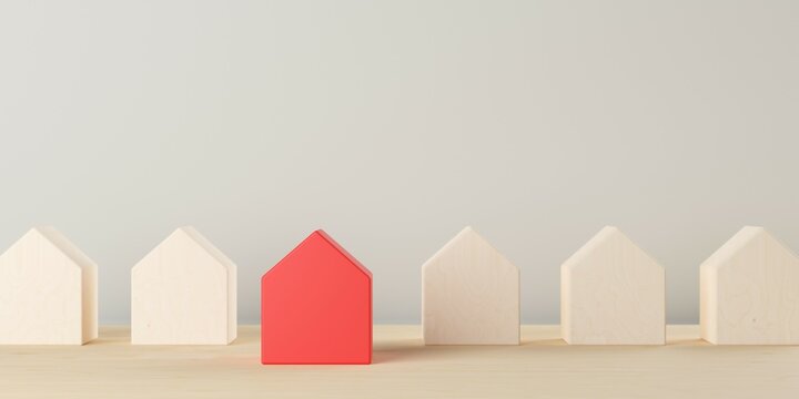 Row of small wooden houses on table background with one red standing out, real estate or housing concept