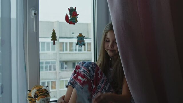 Smiling little girl glues magic stickers of animals on the window, decorates for the holiday.