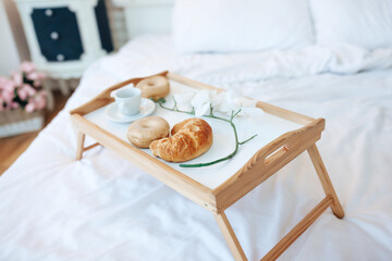 Elegant Provence tasty breakfast in bed. French croissant, coffee and flowers.  Morning mood. Provence interior. Selective focus.