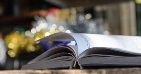 The open book, illuminated by the sun, lies on the table. Bookshelf background and blurry color spots.